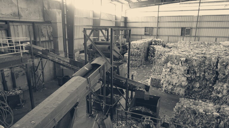 Conveyors inside a materials recovery facility lead toward towering bales of compressed paper and plastic waste.