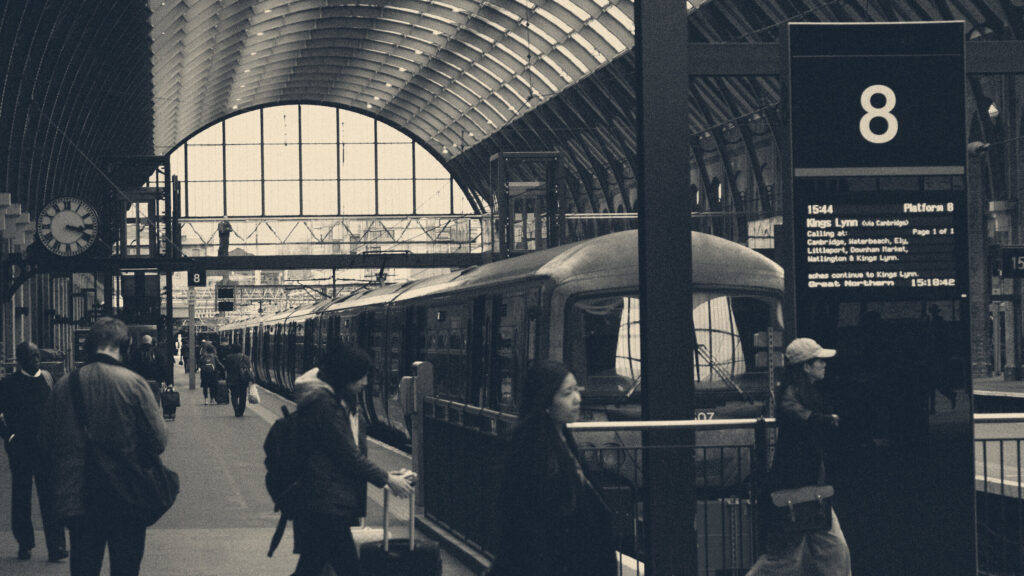 Commuters walking along a platform past a train beneath the arched roof of London Kings Cross station