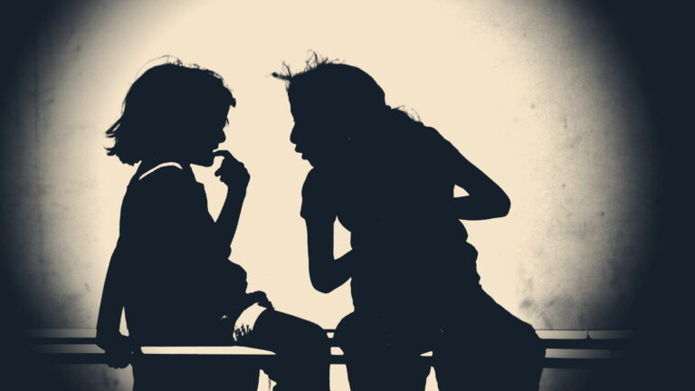 Two silhouetted people lean close on a bench, one whispering into the other's ear against a backlit wall.