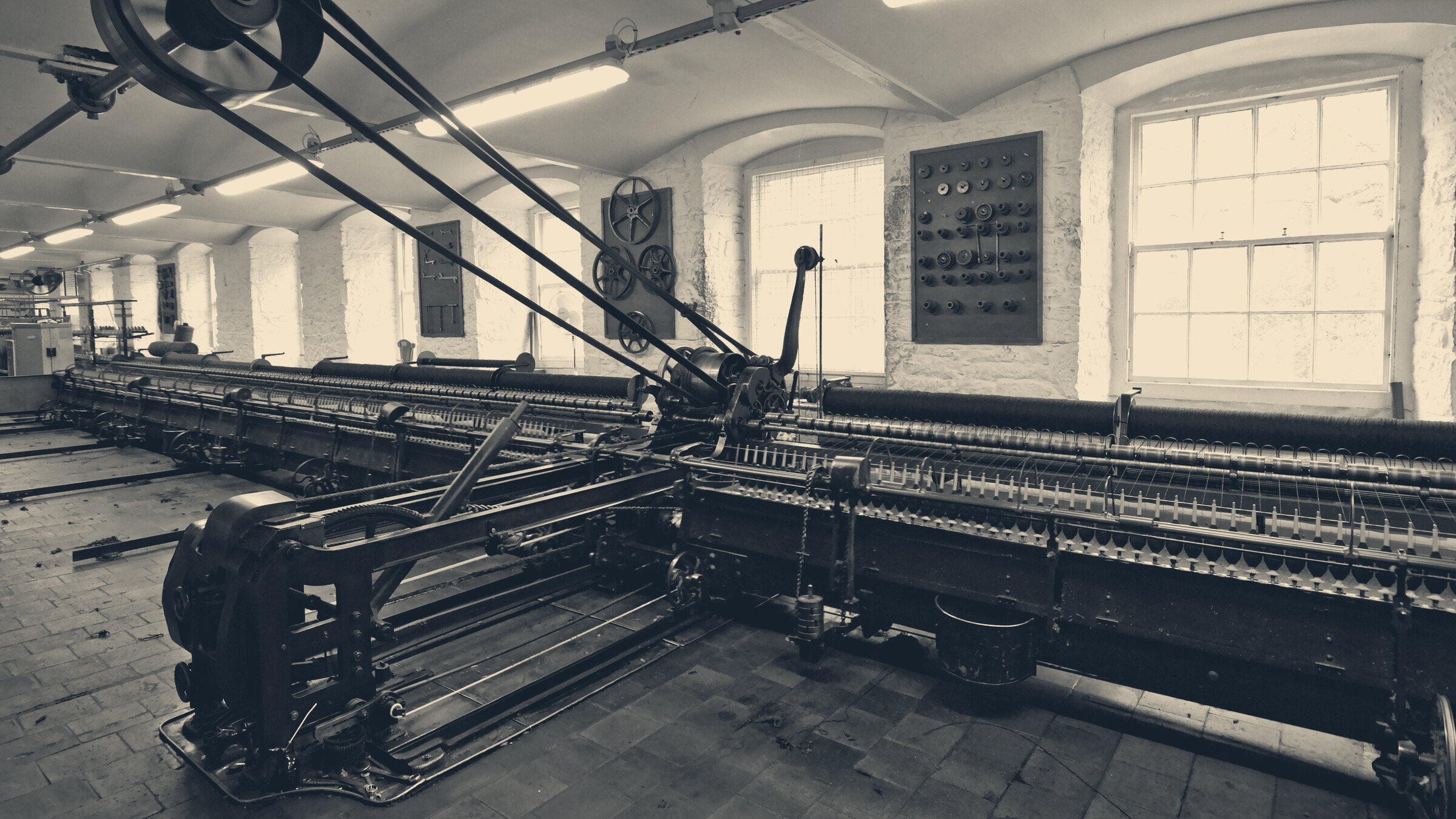 Historic cotton mill spinning mule with drive belts and spindle carriages under arched windows at New Lanark