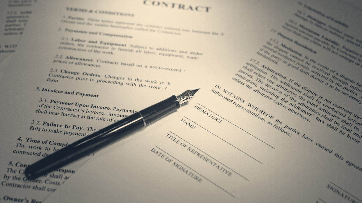 A fountain pen lies unsigned across a printed contract, its nib resting beside empty signature, name and date fields.