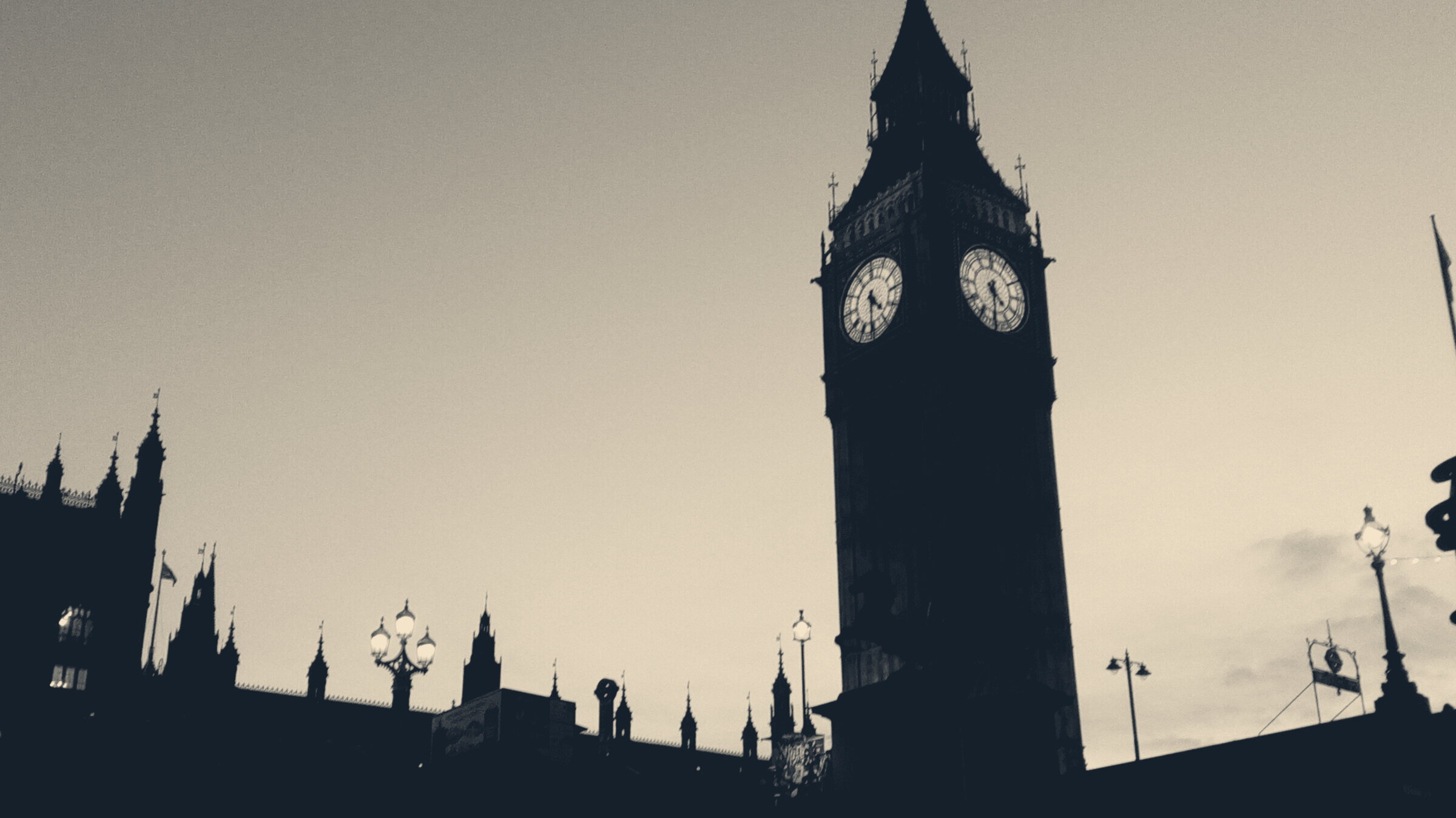 Elizabeth Tower and the Palace of Westminster silhouetted at dusk, the clock face glowing above lit street lamps.