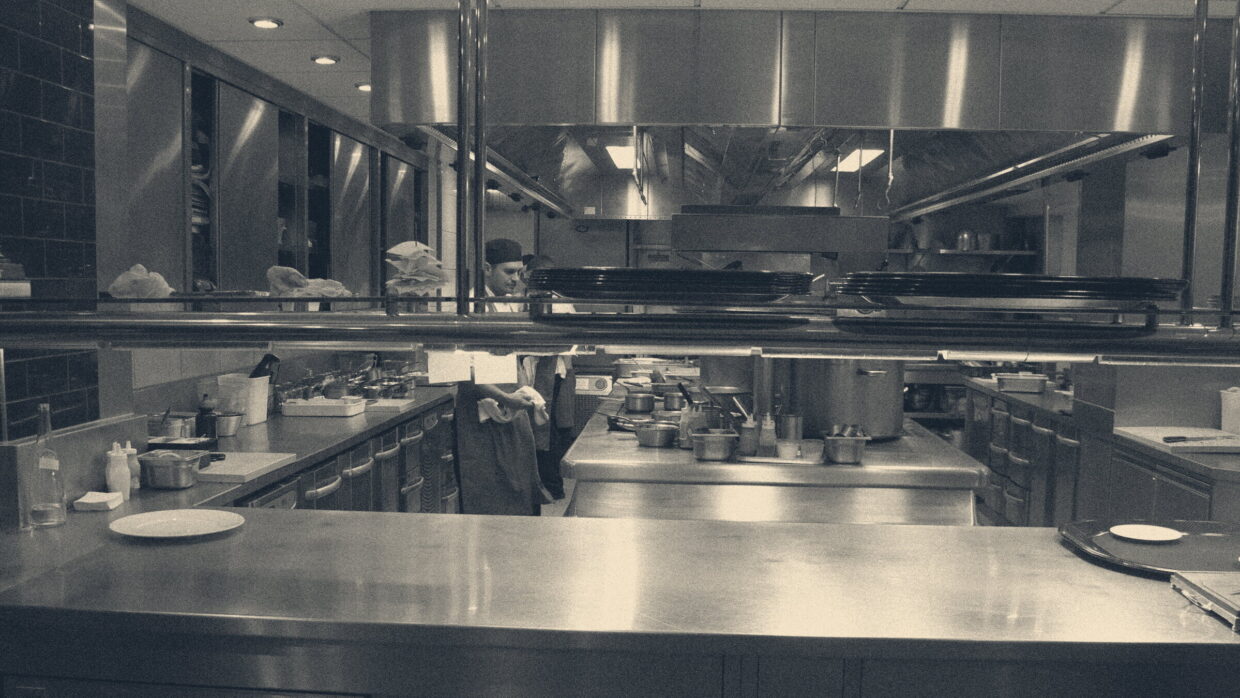 Commercial kitchen pass with order tickets, stainless steel counters, and a chef at work in a London restaurant